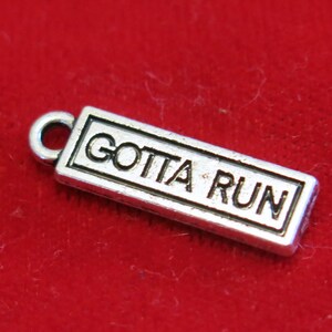 May include: Silver charm with a rectangular shape and the words "Gotta Run" engraved on it.