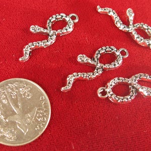 May include: Four silver snake charms with a textured surface. The charms are in the shape of a snake curled up with its tail in its mouth. The charms have a loop at the top for attaching to a necklace or bracelet.