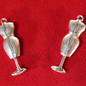 May include: Two silver-toned metal dress form charms with a stand. The charms are detailed with a seam down the front of the dress form.