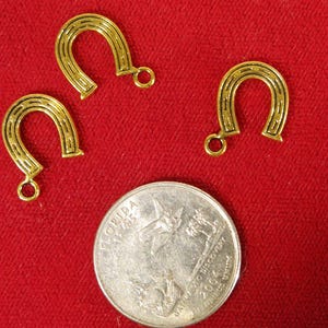 May include: Three gold-colored horseshoe charms with a loop at the top. The charms are on a red surface.