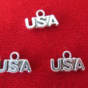 May include: Three silver charms with the word "USA" on them. The charms are on a red background.