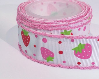 Op de afbeelding: Een rol wit grosgrain lint met een herhalend patroon van rode en roze aardbeien met groene blaadjes, afgewisseld met kleine rode en roze stippen. De randen van het lint zijn afgewerkt met een decoratieve roze geschulpte rand.