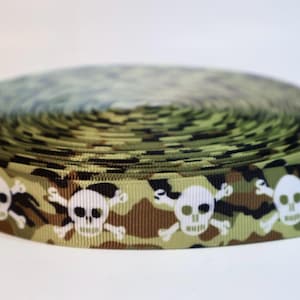 May include: A roll of grosgrain ribbon featuring a camouflage pattern in shades of olive green, brown, and black, accented with a repeating white graphic print of skulls and crossbones arranged horizontally along the length of the fabric.