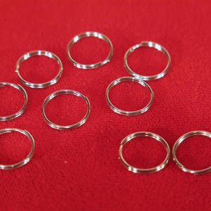 May include: A set of ten silver key rings, all the same size, arranged on a red surface.