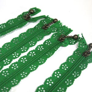 May include: Four green lace zipper pulls with antique brass zipper sliders. The zippers are approximately 10 inches long.