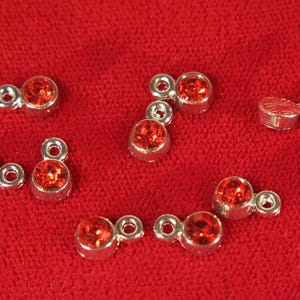 May include: Assortment of red rhinestone charms with silver metal settings. The charms are shaped like Mickey Mouse ears and have a loop for attaching to a necklace, bracelet, or other jewelry.