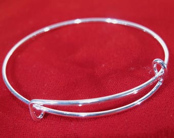 May include: A silver-toned expandable bangle bracelet featuring a thin, circular wire design with two overlapping ends that slide through small loops, allowing the diameter to adjust for a comfortable fit around the wrist.