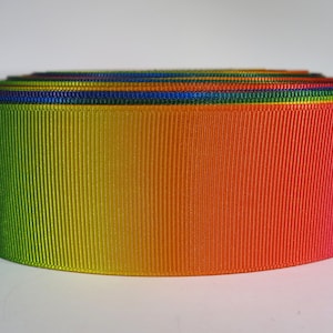 May include: A roll of rainbow ombre ribbon with a green to red gradient. The ribbon is made of a textured fabric with a slight sheen.