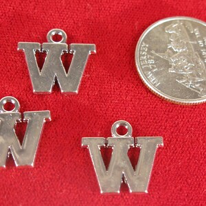 May include: Three silver charm pendants shaped like the letter W. The charms are on a red background.