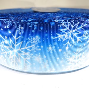 May include: A roll of blue and white ribbon with a snowflake pattern. The ribbon has a gradient from dark blue to white.