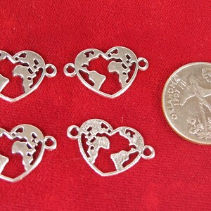 May include: Four silver heart-shaped charms with an outline of the world inside. The charms have two jump rings on each side for attaching to jewelry.