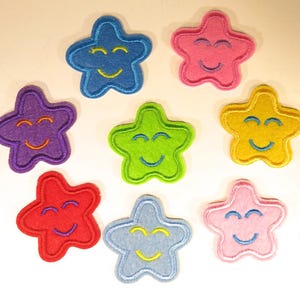May include: A collection of eight star-shaped felt patches in various colors including blue, pink, purple, lime green, yellow, red, light blue, and light pink. Each star features an embroidered smiling face with closed eyes and a curved mouth.