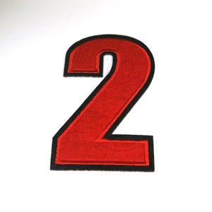 May include: A red number 2 patch with a black border. The number is in a bold, blocky font, and the patch is likely made of felt or a similar material. The background is plain white.