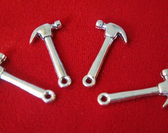 May include: Four silver-colored hammer charms with a loop at the end of the handle. The charms are on a red surface.
