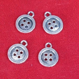 May include: Four silver-toned metal button charms with four holes each. The charms are on a red background.