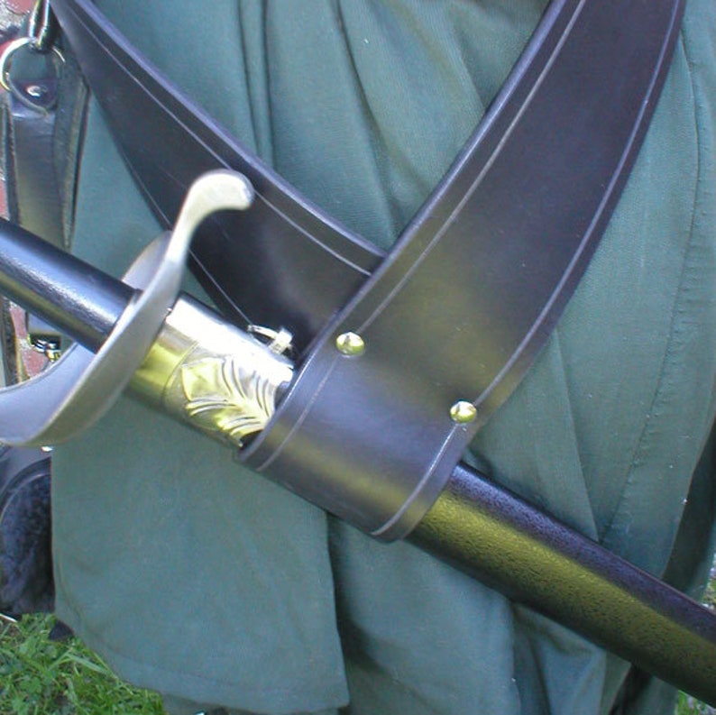 May include: A black leather sword scabbard with a silver-colored metal hilt and a black sword blade. The scabbard is worn diagonally across the body and secured with a strap.