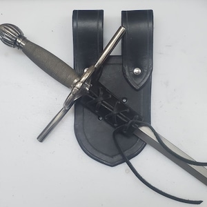 May include: A black leather scabbard with a silver dagger with a decorative pommel. The scabbard has a strap and buckle for attaching to a belt.