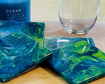 May include: Four square coasters with a blue, green and white marbled design. The coasters are made of resin and have a glossy finish.