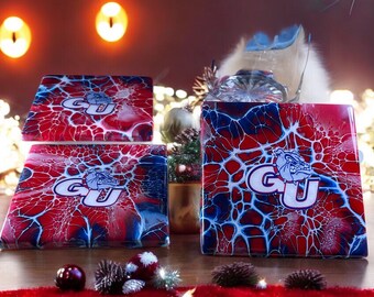 May include: Set of four coasters with an abstract design in red, white and blue. The coasters feature a white "GU" logo with a bulldog mascot.