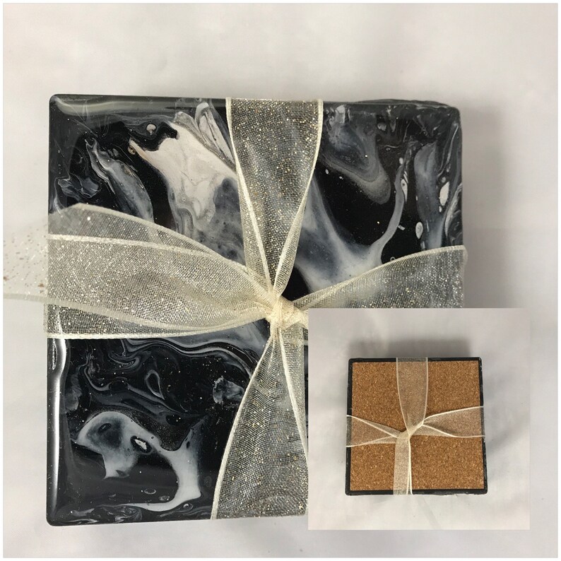 May include: Set of four black and white marble coasters with a white ribbon tied around them. The coasters are made of resin and have a glossy finish.