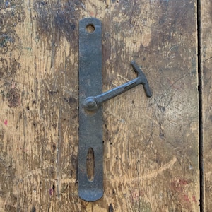 Puede incluir: Un pestillo de puerta de metal negro rústico con una manija de palanca. El pestillo está montado en una puerta de madera.