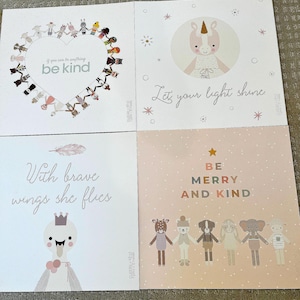 May include: Four square cards with illustrations and text. One card has a heart shape with the words "be kind". Another says "Let your light shine" with a unicorn illustration. A third says "With brave wings she flies". The last says "Be Merry and Kind".