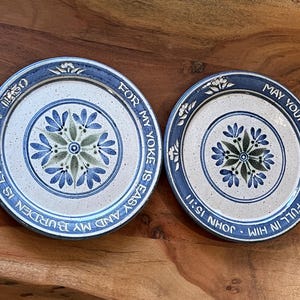 May include: Two round ceramic plates with a speckled cream center and blue rim. The larger plate features a blue floral pattern and the text FOR MY YOKE IS EASY AND MY BURDEN IS LIGHT MT 11:30. The smaller plate has a blue floral pattern and MAY YOUR JOY BE MADE FULL IN HIM JOHN 15:11.