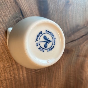 Puede incluir: Jarr&oacute;n de cer&aacute;mica blanco con un logotipo azul y blanco que dice "Emerson Creek Pottery, Va. 2010, Beadhollow."