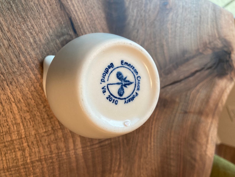 Puede incluir: Jarr&oacute;n de cer&aacute;mica blanco con un logotipo azul y blanco que dice "Emerson Creek Pottery, Va. 2010, Beadhollow."