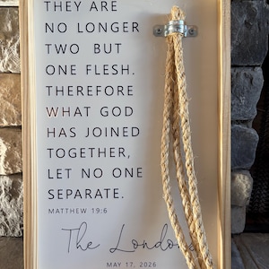 Puede incluir: Cartel enmarcado en madera con el texto "THEY ARE NO LONGER TWO BUT ONE FLESH. THEREFORE WHAT GOD HAS JOINED TOGETHER, LET NO ONE SEPARATE." y "MATTHEW 19:6". Incluye "The London" y la fecha "MAY 17, 2026". Cuenta con una cuerda para colgar.