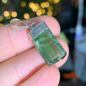May include: A silver pendant with a green gemstone. The gemstone is a rectangular shape with a faceted cut. The pendant is on a white background.