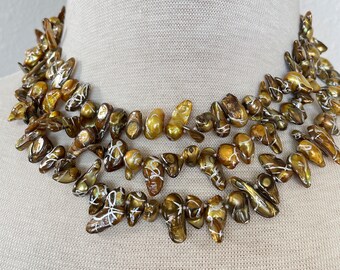 May include: A multi-strand necklace made of brown baroque pearls with white accents. The pearls are irregular in shape and size, creating a unique and elegant look.