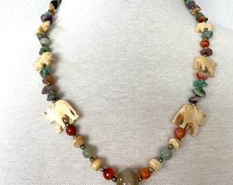 May include: A multi-colored beaded necklace with carved ivory elephant charms. The necklace features green, red, brown, and beige beads with a large agate stone in the center.
