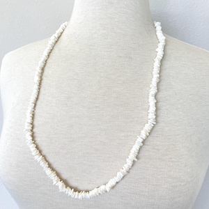 Puede incluir: Un collar de conchas blancas hecho de pequeñas piezas cuadradas. El collar está en un maniquí blanco.