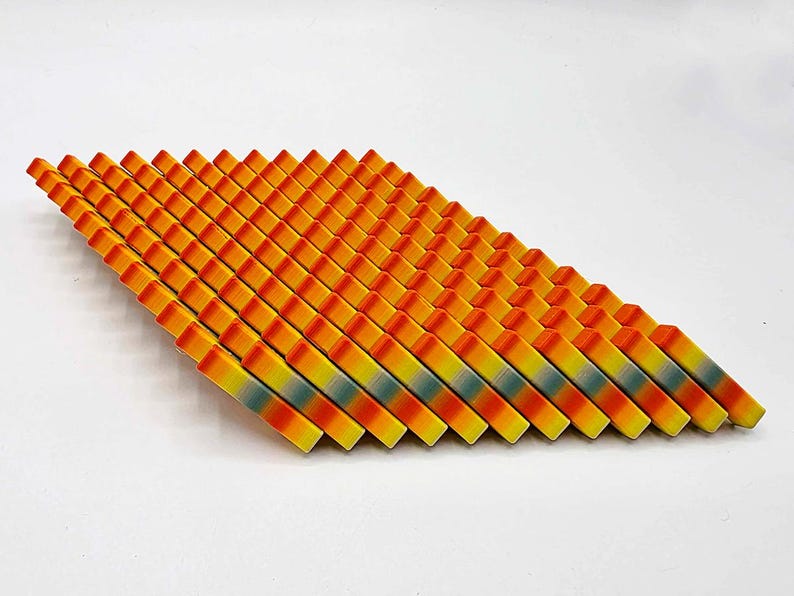 May include: A collection of colorful, geometric wooden blocks arranged in a diagonal pattern. The blocks transition from orange to yellow, with a hint of blue-green in the middle. The arrangement is on a white background.