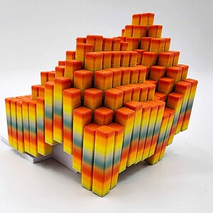 May include: A geometric sculpture composed of numerous rectangular blocks. The blocks are arranged in a stepped, pyramid-like formation. The color gradient transitions from yellow to orange, with hints of blue and green.