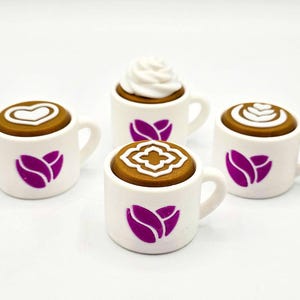May include: Four miniature white coffee mugs with brown coffee and decorative foam toppings. Each mug has a purple tulip design. The coffee art includes a heart, a flower, and a swirl. The mugs are on a white surface.