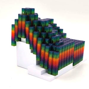 Peut inclure: Une sculpture abstraite colorée composée de nombreux blocs rectangulaires disposés en forme d'escalier. Les blocs présentent un dégradé de couleurs, notamment orange, vert et bleu. La sculpture est montée sur une base blanche en escalier.