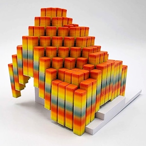 May include: A colorful, abstract sculpture composed of numerous rectangular blocks. The blocks are arranged in a stepped, pyramid-like structure, with a gradient of colors from orange to yellow to green. The base is white.