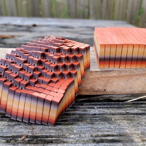 Peut inclure: Une grande pile de blocs rectangulaires colorés, composés de couches de nuances d'orange, de brun et de jaune. Les blocs sont disposés en quinconce, créant un motif géométrique texturé.