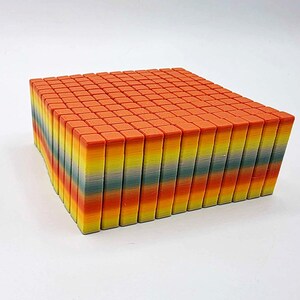 May include: A rectangular block composed of numerous small, colorful, rectangular pieces. The top surface is a solid orange, while the sides reveal a gradient of colors including yellow, green, and orange. The object is set against a white background.
