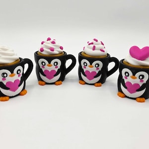 May include: Four black mugs shaped like penguins, each with a different topping. The penguins have white faces, pink hearts, and orange feet. The toppings include whipped cream, sprinkles, and a pink heart.