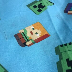 Puede incluir: Tela azul con un patr&oacute;n repetido de personajes de Minecraft. Los personajes incluyen a Steve, Alex y un Creeper.