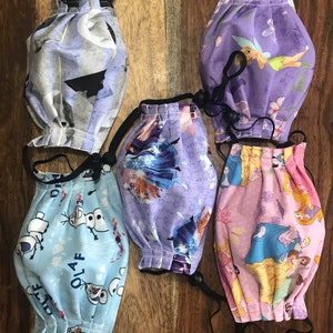 May include: Five different fabric face masks with various Disney character prints. The masks are all blue, purple, or pink with white accents. The masks have black elastic ear loops and a black drawstring for adjusting the fit.