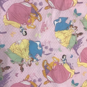 Puede incluir: Tela rosa con un patr&oacute;n repetido de princesas Disney en sus ic&oacute;nicos vestidos. Las princesas incluyen Cenicienta, Blancanieves, Bella, Ariel y Rapunzel. La tela est&aacute; decorada con mariposas y un castillo.