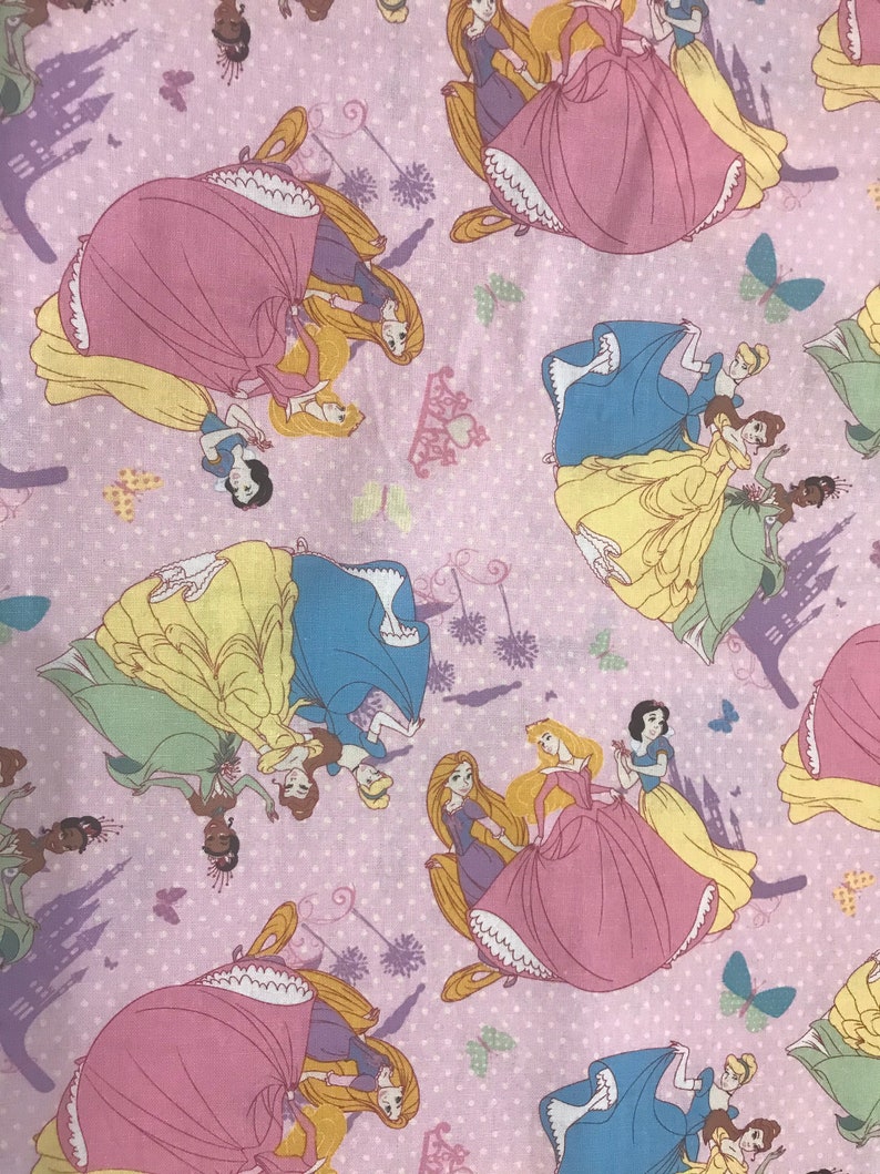 Puede incluir: Tela rosa con un patr&oacute;n repetido de princesas Disney en sus ic&oacute;nicos vestidos. Las princesas incluyen Cenicienta, Blancanieves, Bella, Ariel y Rapunzel. La tela est&aacute; decorada con mariposas y un castillo.