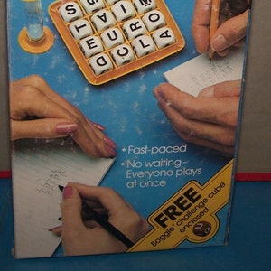 May include: A blue and yellow game box for the word game Boggle. The box features a photo of the game board with letter tiles, a timer, and two hands writing down words on paper. The text on the box reads "Parker Brothers Boggle The 3-Minute Word Game".