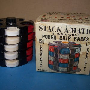 May include: A black Stack-A-Matic poker chip rack with red, white, and blue chips. The box next to it reads "STACK-A-MATIC POKER CHIP RACKS" and "150 POKER CHIPS". The rack holds 150 poker chips.