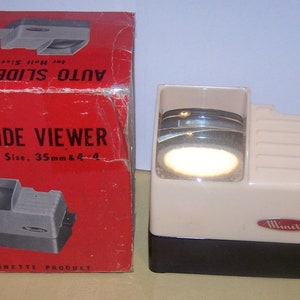 May include: A white and black Minolta Auto Slide Viewer for 35mm slides. The viewer is in its original box, which is red with black trim. The box has the text "Auto Slide Viewer" printed on it.
