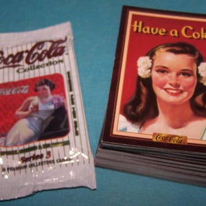 May include: A pack of Coca-Cola collectible cards featuring a vintage illustration of a woman with the text "Have a Coke".